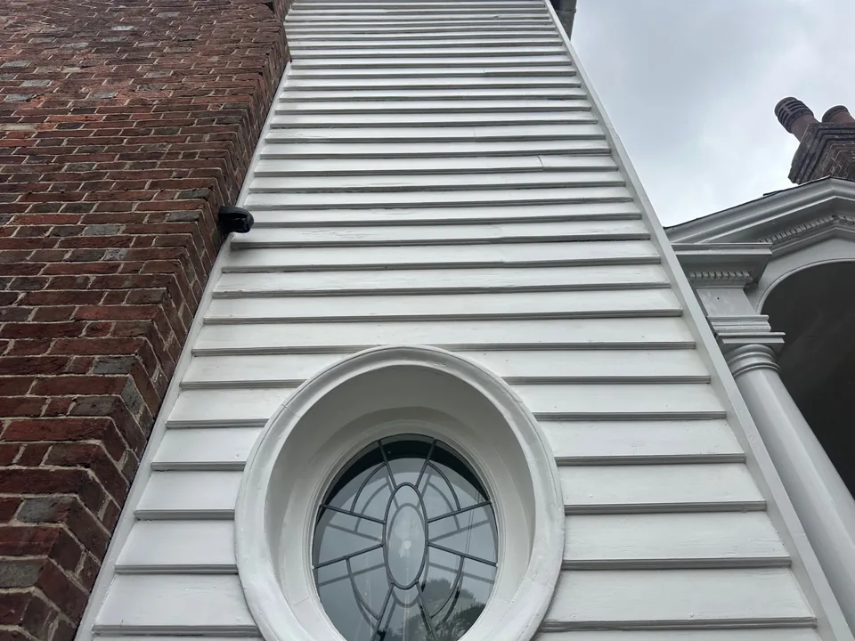 White-clad gable above a circular leaded window beside a brick wall.