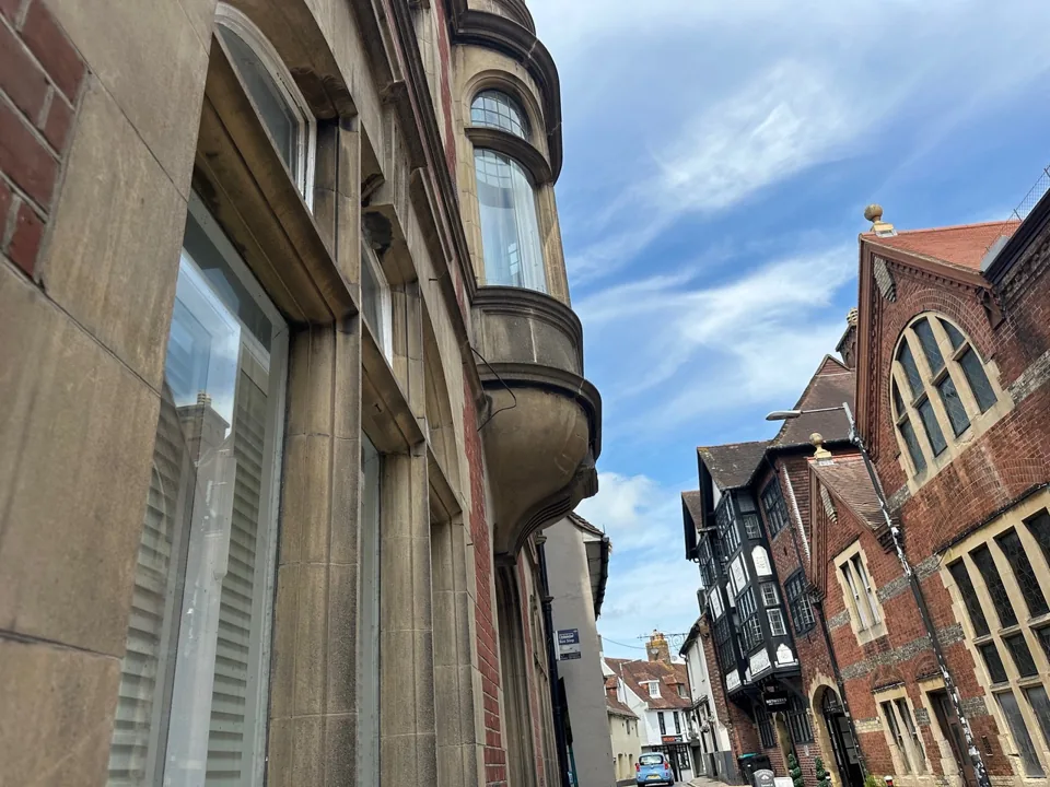 Curved projecting bay window above a narrow street of period buildings.