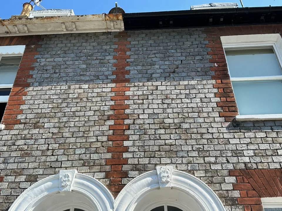 Flint-faced elevation with brick bands and decorative arched window surrounds.