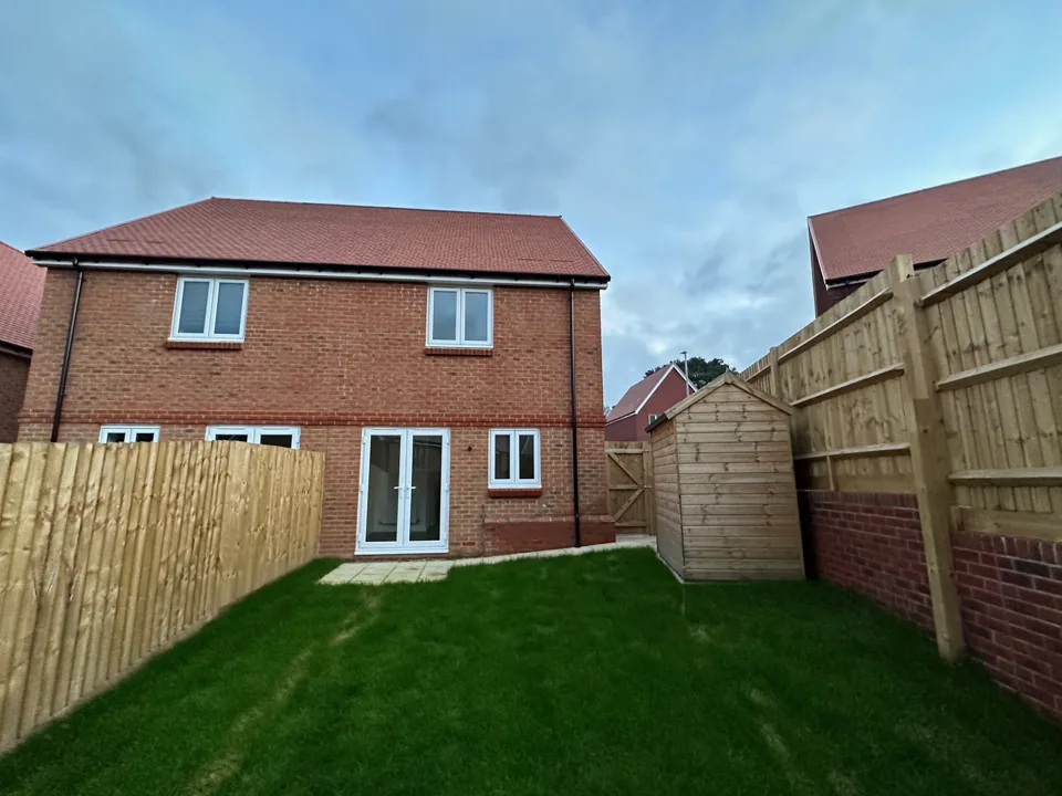 Rear elevation of a modern brick house overlooking an enclosed lawn.